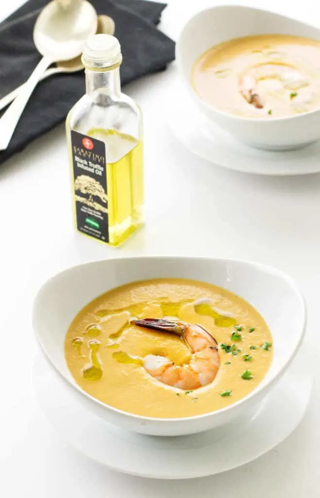 Overhead view of two bowls of shrimp bisque, bottle of truffle oil, napkins and spoons
