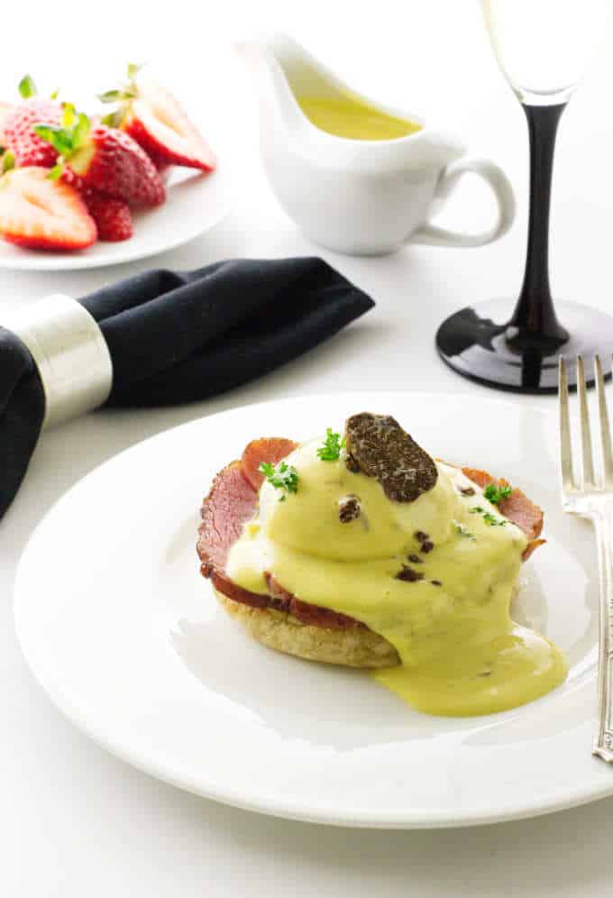 Eggs Benedict with White Truffled Hollandaise Sauce and a plate of strawberries.