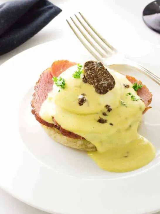 Eggs Benedict with White Truffled Hollandaise Sauce and a slice of a truffle.