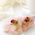 two heart shaped Valentine's Day cookies on a plate, cup of coffee and napkin in background