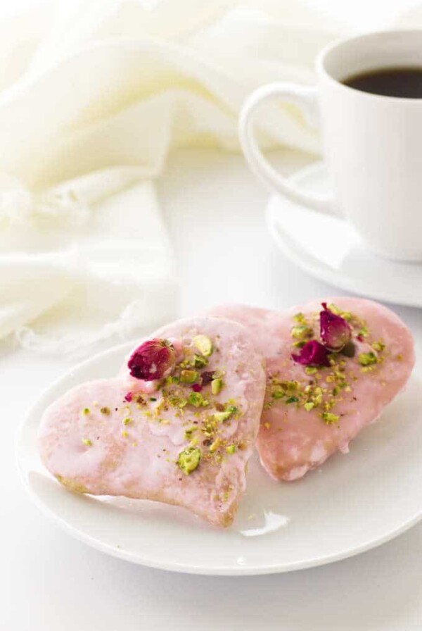 two heart shaped Valentine's Day cookies on a plate, cup of coffee and napkin in background