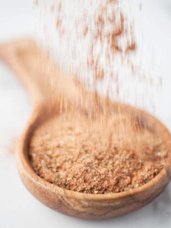 Cajun seasoning mix being sprinkled into a wooden spoon.