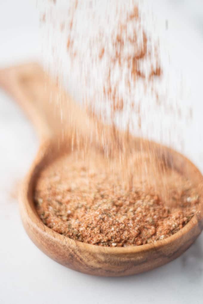 Cajun seasoning mix being sprinkled into a wooden spoon.