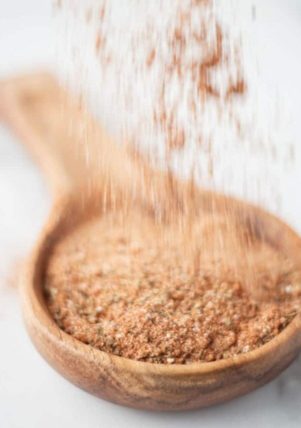 Cajun seasoning mix being sprinkled into a wooden spoon.