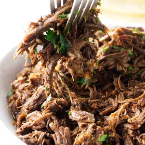 Shredded beef being scooped with a couple of forks.