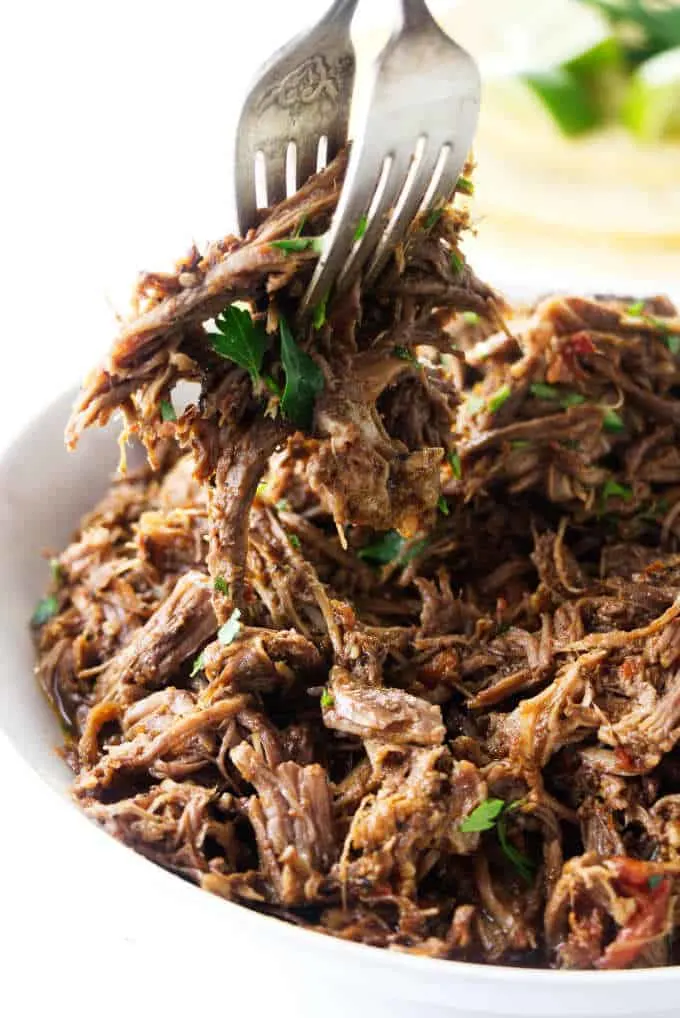 Shredded beef being scooped with a couple of forks.