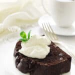 Slice of chocolate loaf cake on a serving plate with fork, coffee and napkin in background