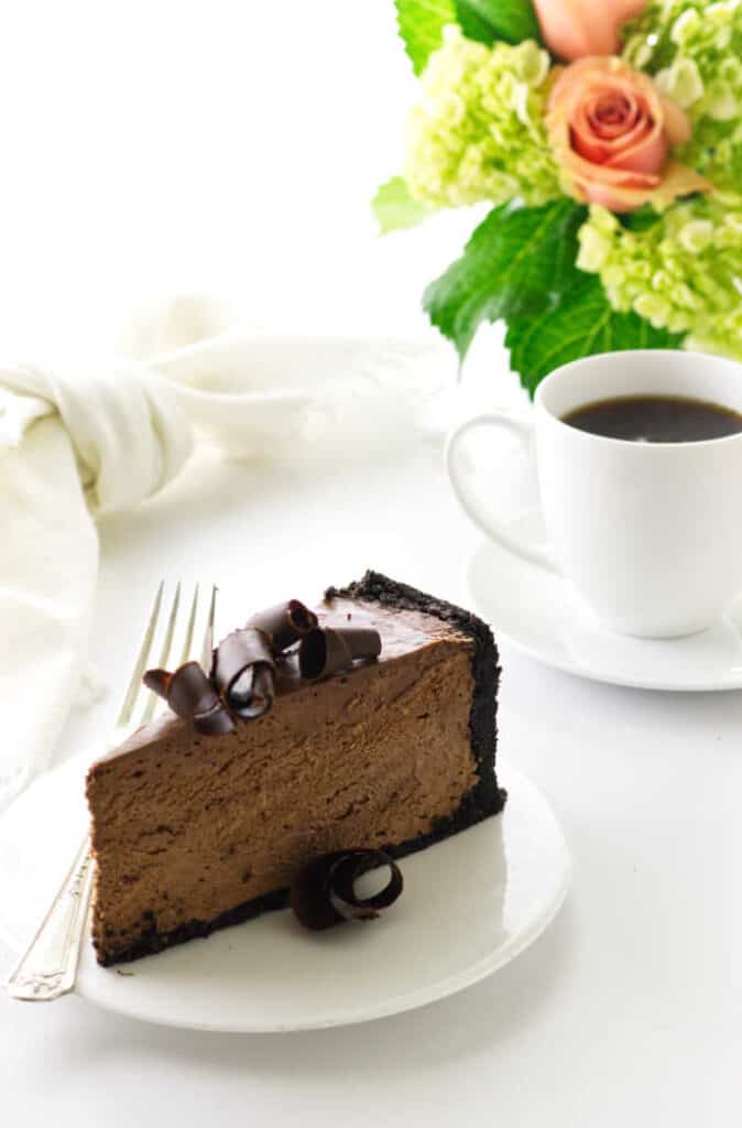 Serving of chocolate no bake cheesecake, coffee with napkin and flowers in background