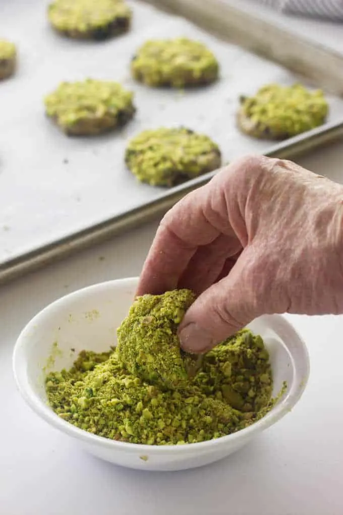 Dipping cookie dough into chopped pistachios.
