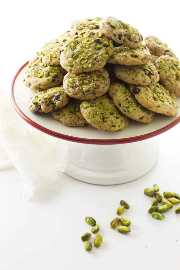 A serving platter with pistachio cherry cookies and some pistachio nuts.