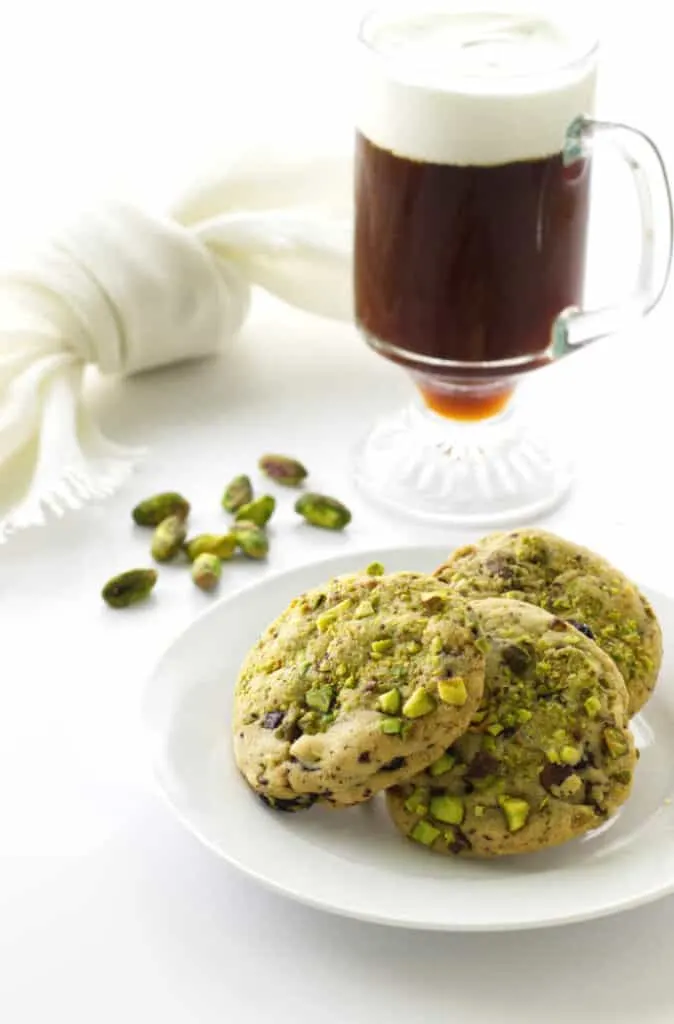 A plate filled with 3 pistachio cherry cookies and a latte drink in the background.