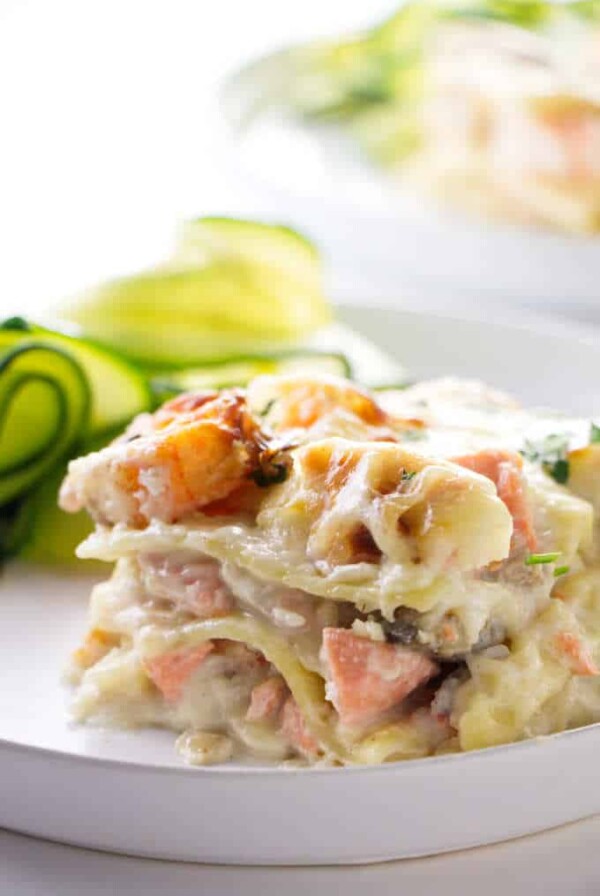 A slice of seafood lasagna with zucchini in the background.