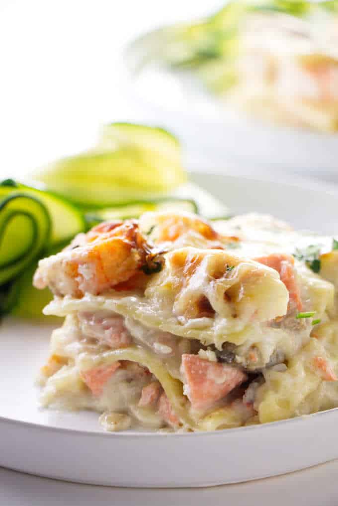 A slice of seafood lasagne with zucchini in the background.