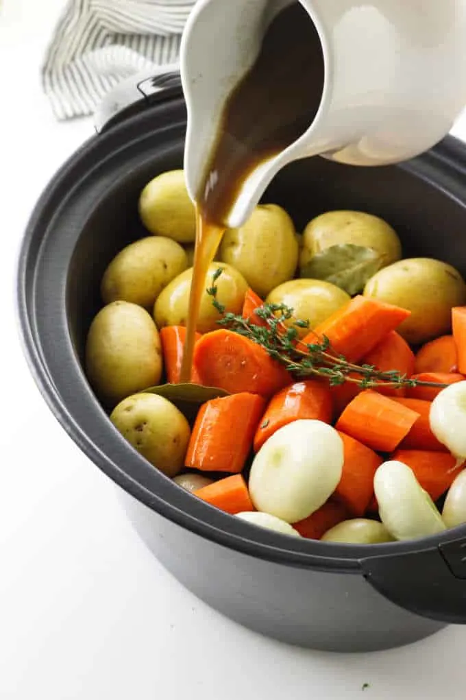 Vegetables in slow cooker with beef broth pouring on