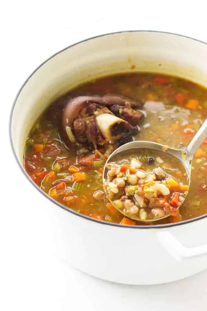 Overhead view of a soup pot of 15 bean soup, ham bone and a ladle of soup