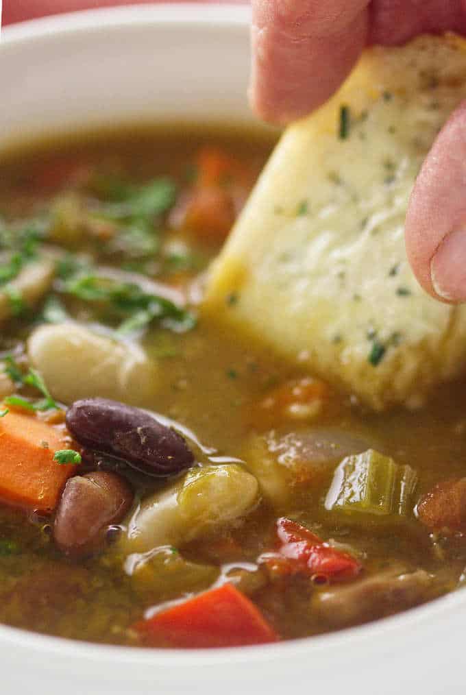 Close up view of a serving of soup with bread being dipped into soup