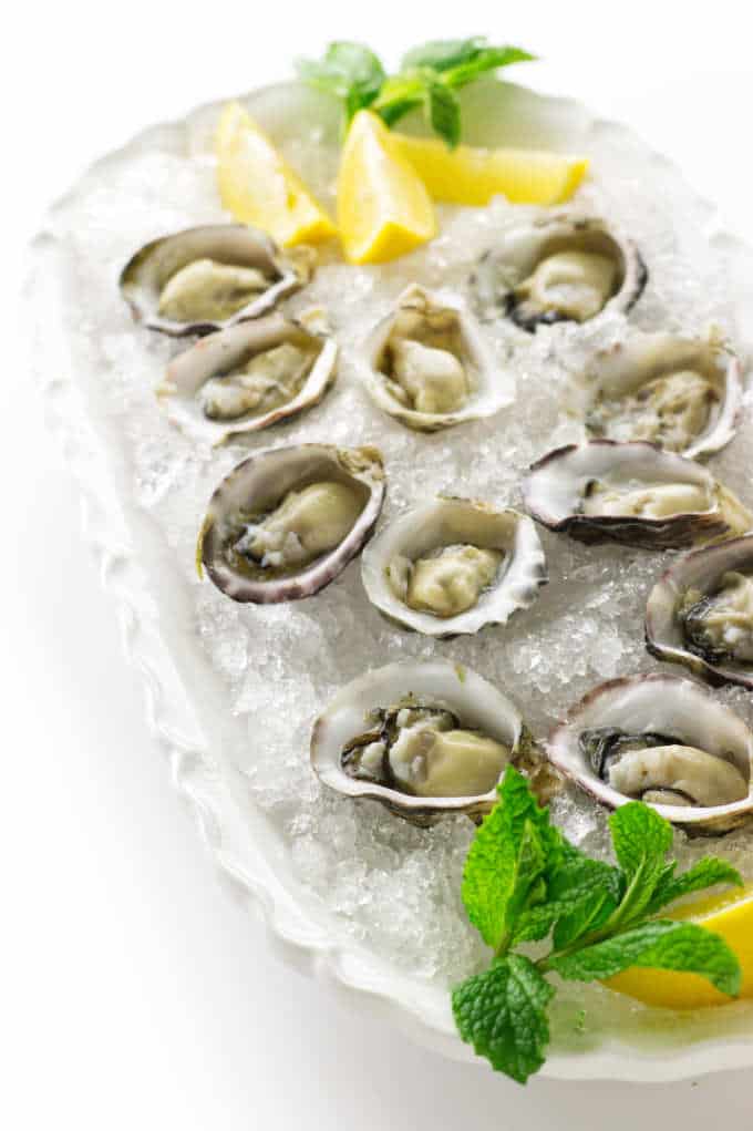 Plate of of oysters on the half shell in a bed of crushed ice, mint and lemon wedges