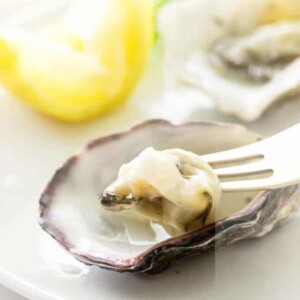 Oysters on appetizer plate, one oyster on fork, lemon wedge in background