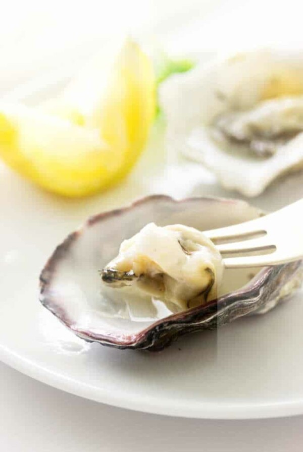 Oysters on appetizer plate, one oyster on fork, lemon wedge in background