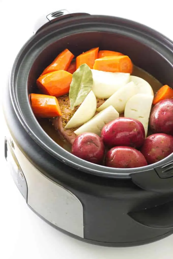 Slow cooker loaded with corned beef, carrots, onions, turnip and a bay leaf