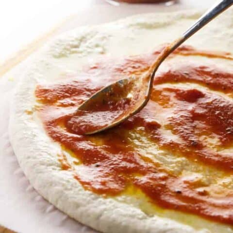 Putting pizza sauce on sourdough pizza dough.