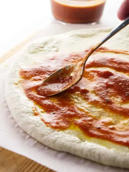 Putting pizza sauce on sourdough pizza dough.