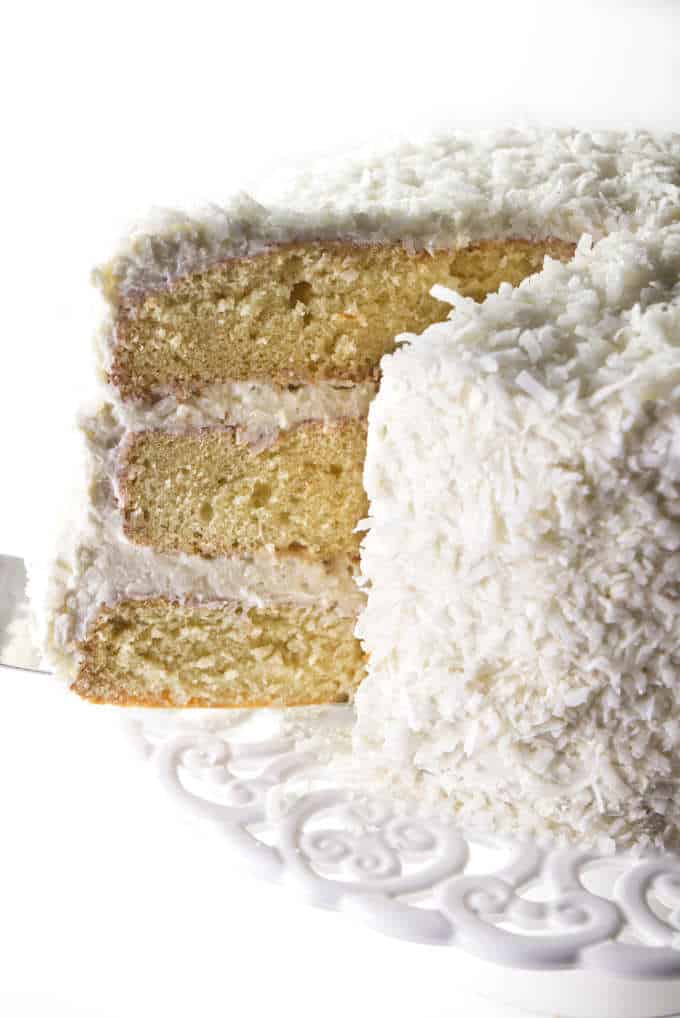 Layered coconut cake with coconut buttercream being served from a cake pedestal.