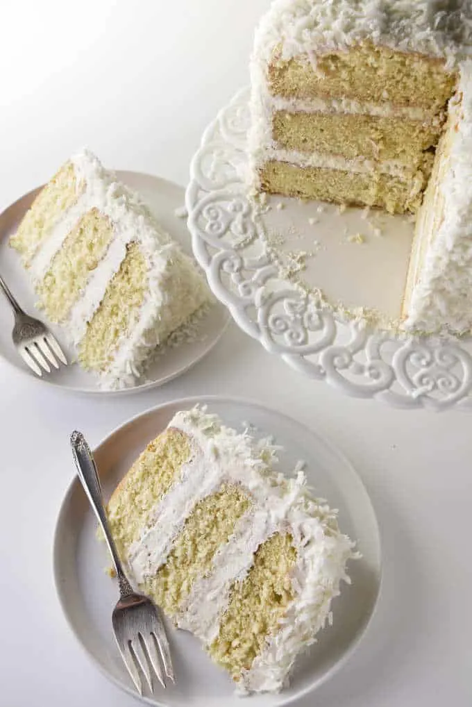 Overhead shot of a layered coconut cake on a cake pedestal along with 2 slices on plates.