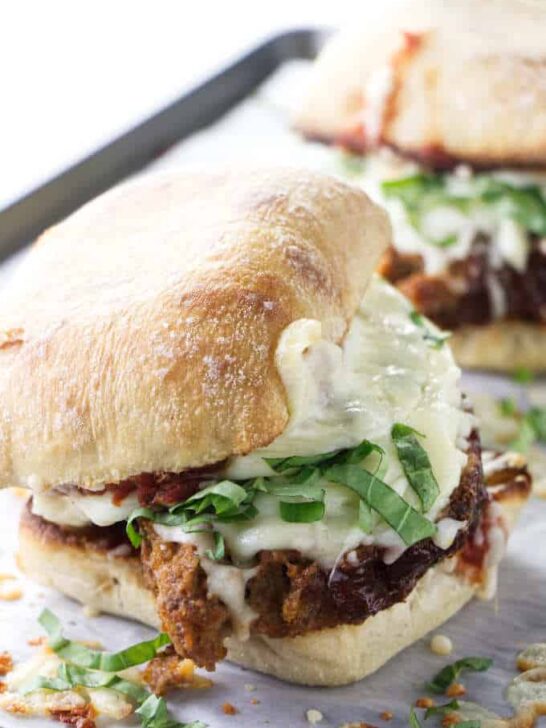 Closeup of a hot meatloaf sandwich with melted cheese and fresh basil.