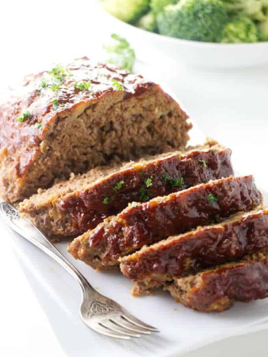 Slices of instant pot meatloaf on a plate with broccoli in the background.