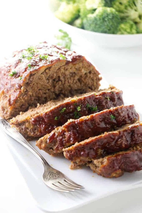 Slices of instant pot meatloaf on a plate with broccoli in the background.