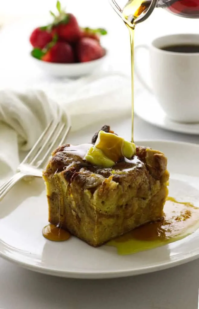 Baked French toast casserole with syrup, coffee and strawberries in bckground