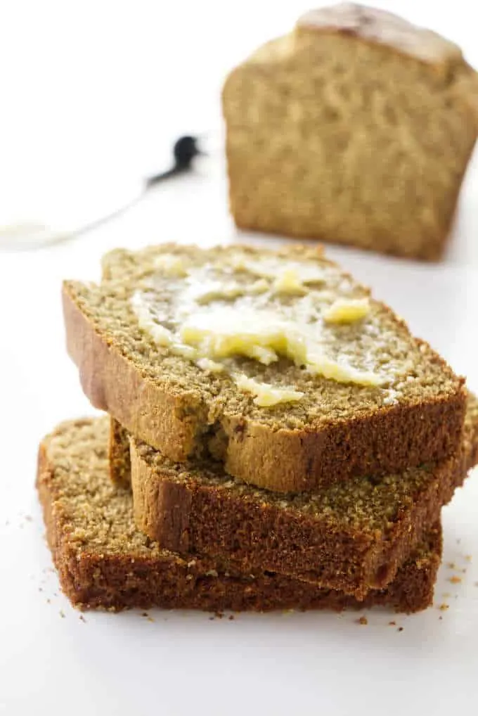 Slices of barley bread with butter and a loaf of bread in the background.