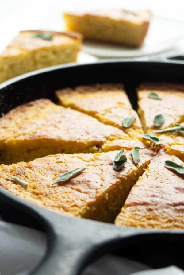 A skillet with sliced cornbread and sage leaves.