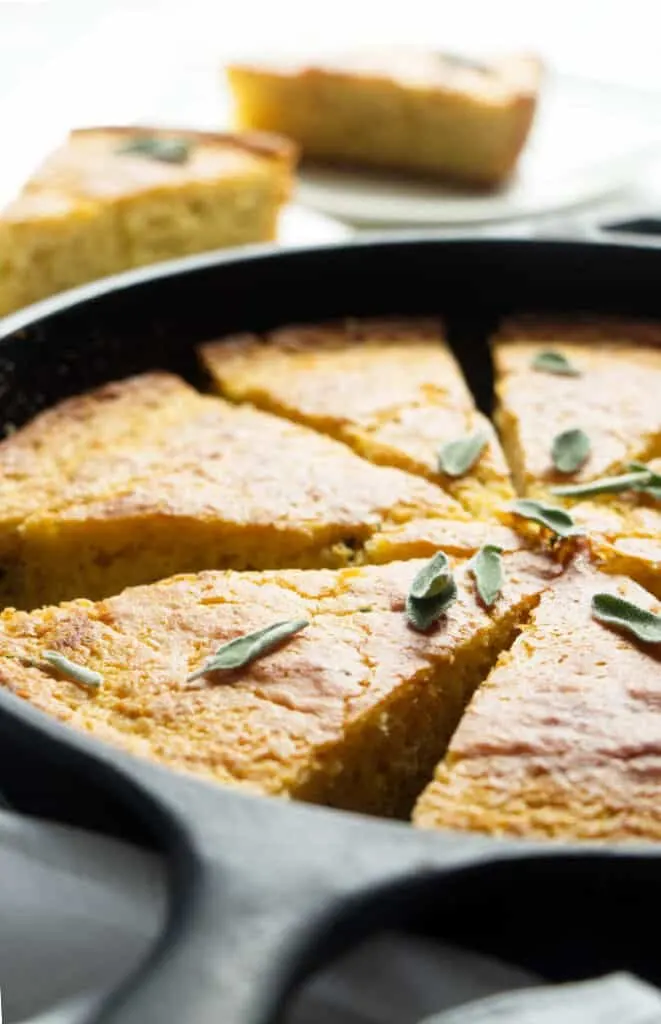 A skillet with sliced cornbread and sage leaves.