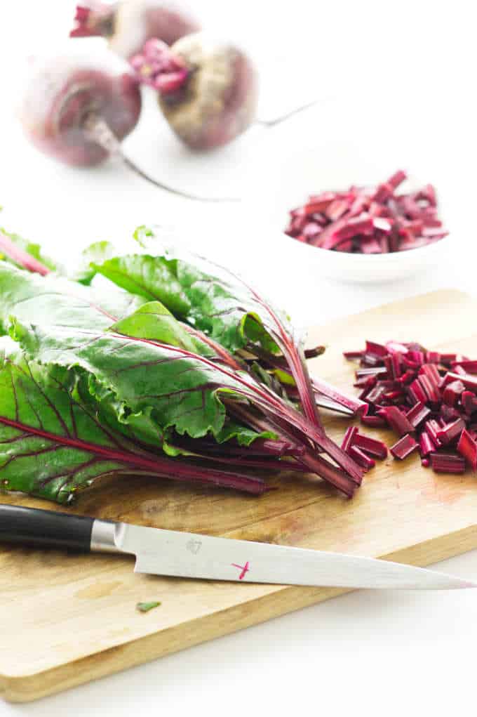 Beet greens being prepped on cutting board, dish of cut stems and whole beets in background