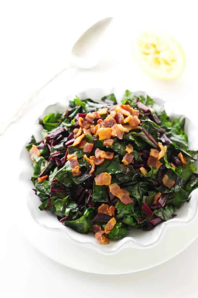 Overhead view of a dish of sautéed beet greens and crisp bacon bits.