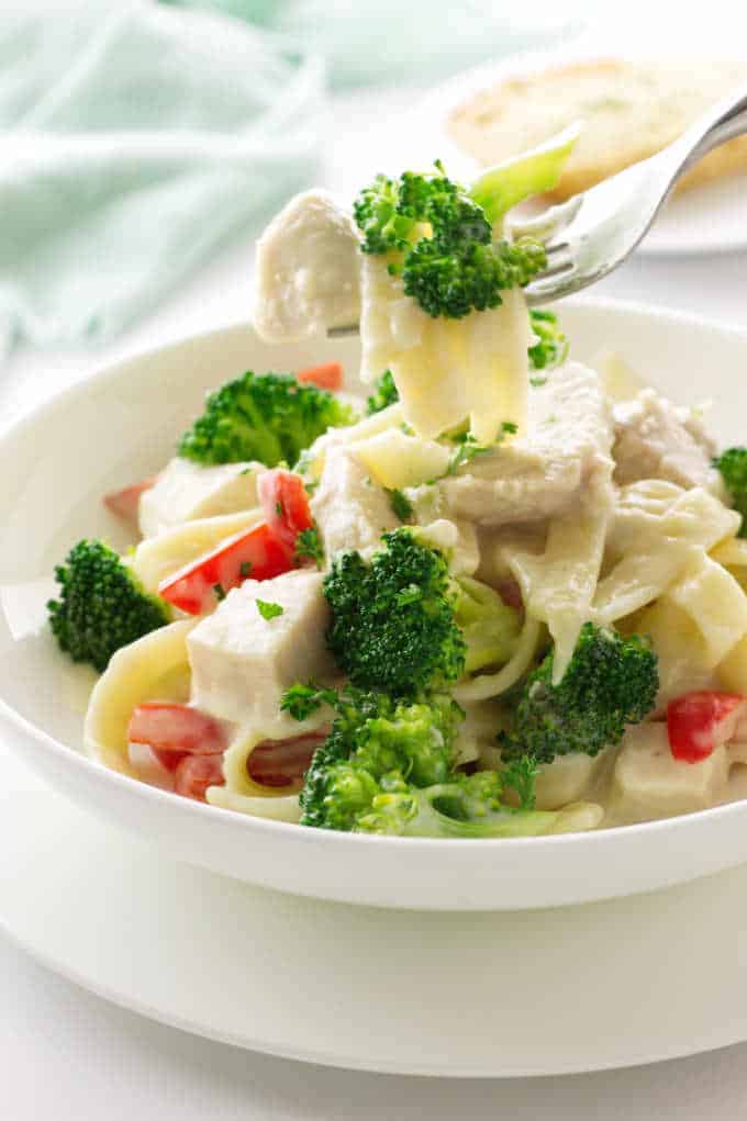 Close up vie of a bite of pasta, chicken and broccoli on a fork