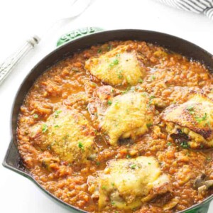 Italian sauce in skillet with chicken thighs. Towel and fork in background