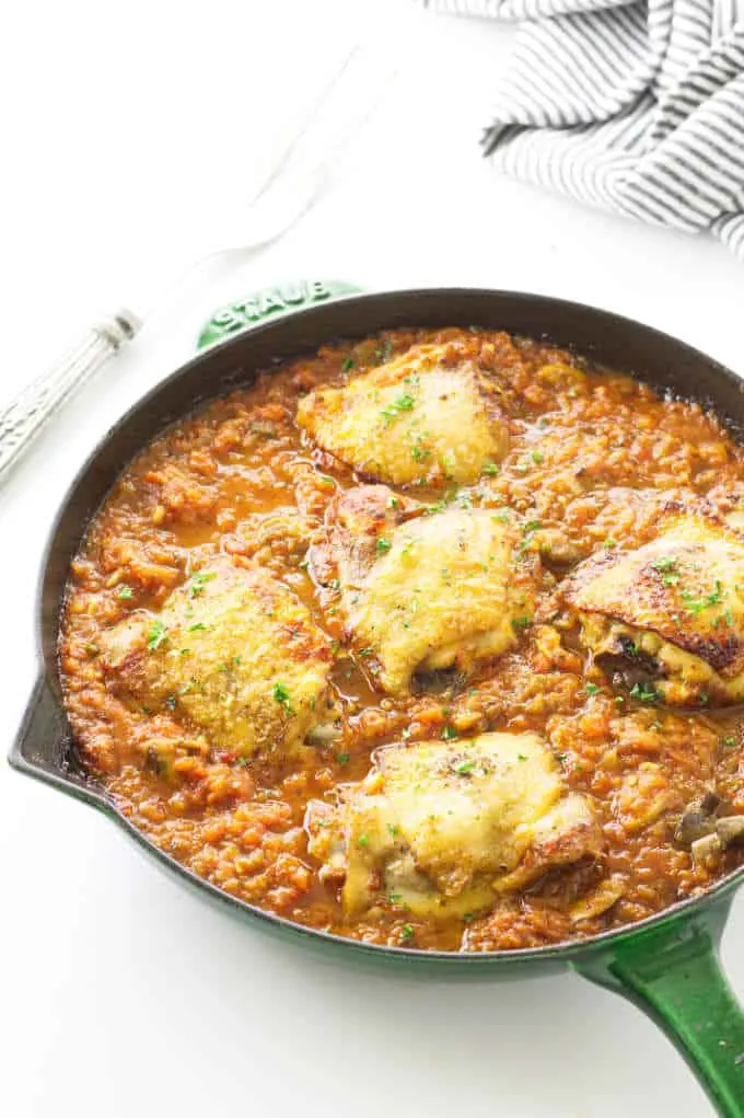 Italian sauce in skillet with chicken thighs. Towel and fork in background