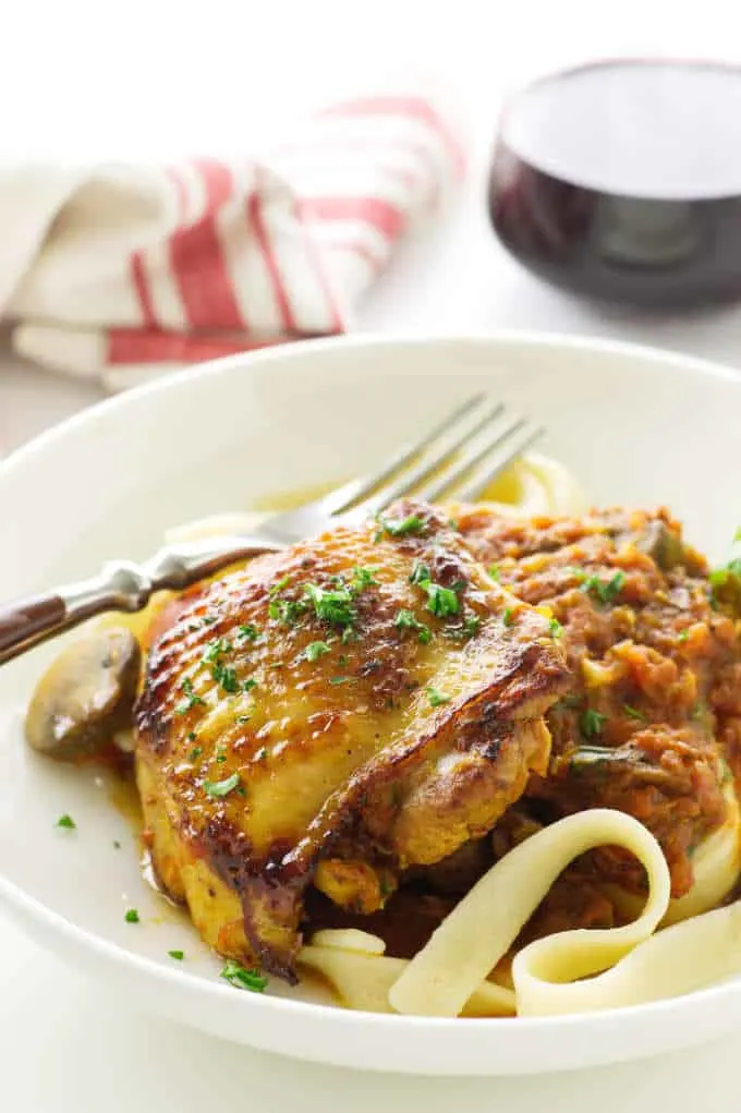 serving of chicken in sauce over pasta. glass of wine and napkin in background