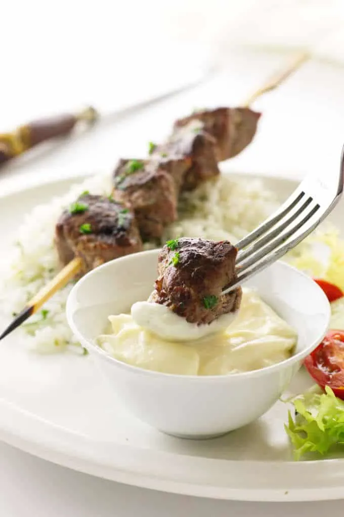 Close up view of lamb kabob on a fork dipped in garlic aioli