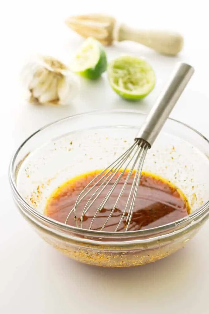 Dish of marinade with whisk. Limes, garlic and juicer in background