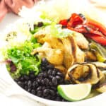 Bowl of black beans, roasted chicken, onions, red/green bell pepper and lime wedge