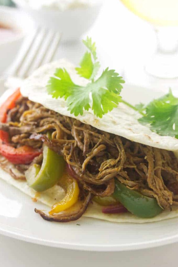 Tri-Tip Fajita and fork on a plate with cilantro sprig beer and condiments in background