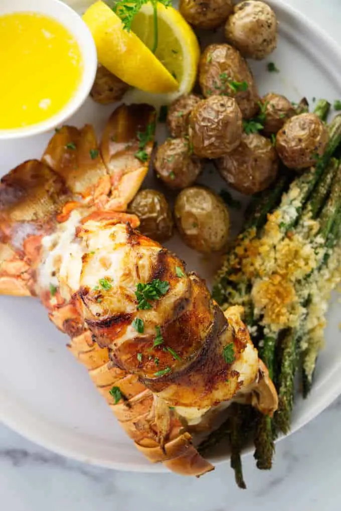 Broiled lobster tail on a plate with potatoes and asparagus.