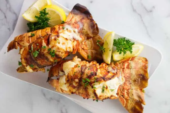 two lobster tails on a plate with lemon wedges.
