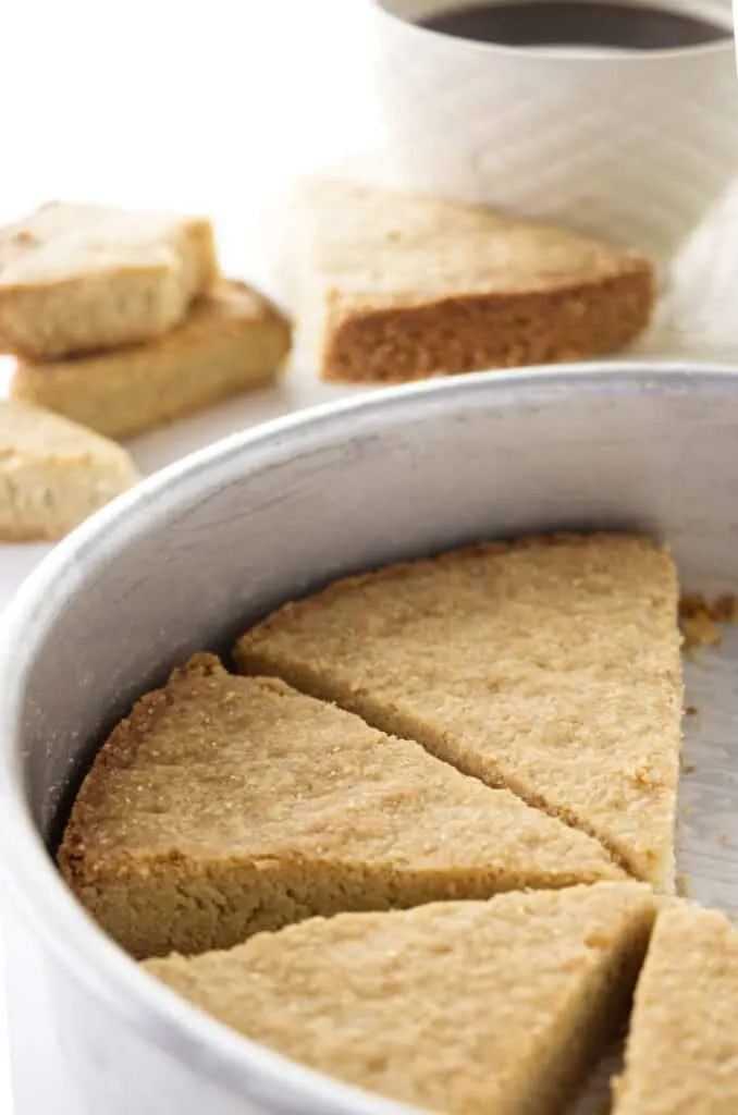 A pan of oatmeal shortbread with coffee in the background.
