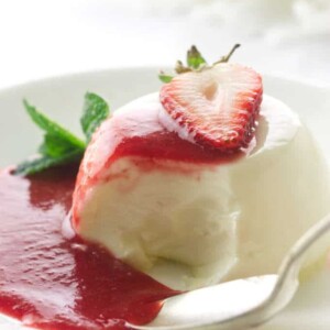 Panna cotta serving with spoon and bite, puddle of strawberry sauce