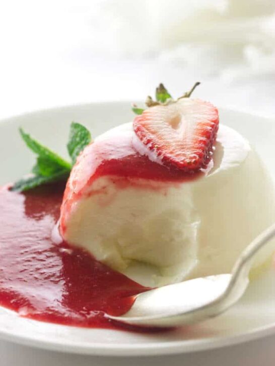 Panna cotta serving with spoon and bite, puddle of strawberry sauce